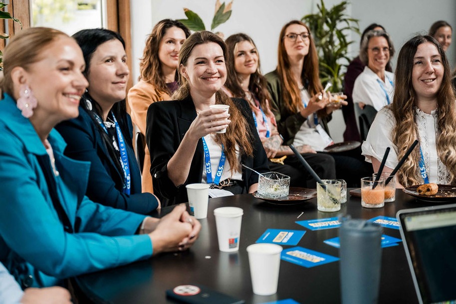Smiling women listening and talking around a table at Supply Chain Women's DELIVER Europe gathering